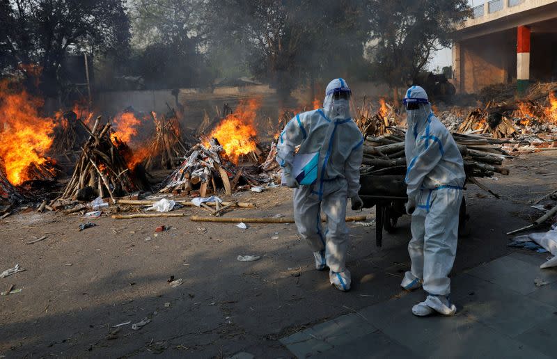 Trabajadores de salud con equipos de protección cargan madera para preparar la cremación de una víctima de COVID-19 en Nueva Delhi, India. Abril 26, 2021. REUTERS/Adnan Abidi