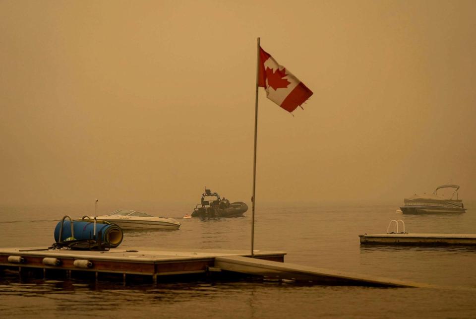 PHOTO: Thick smoke from the Lower East Adams Lake wildfire fills the air around a Canadian flag fluttering in the wind as Royal Canadian Mounted Police officers on a boat patrol Shuswap Lake, in Scotch Creek, British Columbia, Aug. 20, 2023. (Darryl Dyck/AP)