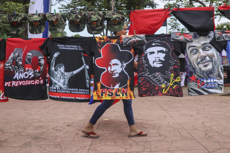 A woman walks past T-shirts for sale promoting The Sandinista National Liberation Front ruling party on the sidelines of a new monument, called the Peace Bell, before its inauguration ceremony later in the day in Managua, Nicaragua, Friday, July 17, 2020. Nicaraguan President Daniel Ortega's government is being deterred by the new coronavirus from holding the usual mass celebration to mark the victory of the country's revolution July 19, and will instead unveil a new addition to its collection of monuments. At right are two T-shirts of Cuba's revolutionary hero Ernesto "Che" Guevara. (AP Photo/Alfredo Zuniga)