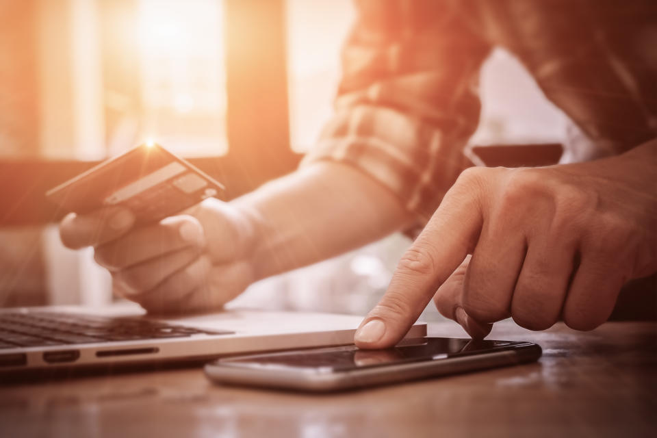 Man holding a credit card with a notebook computer and smartphone in front of him.