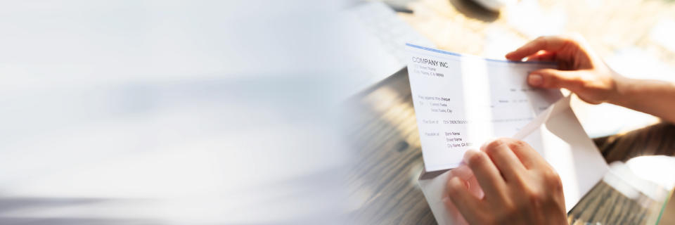 Close-up Of A Businessperson's Hand Opening Envelope With Paycheck Over Wooden Desk