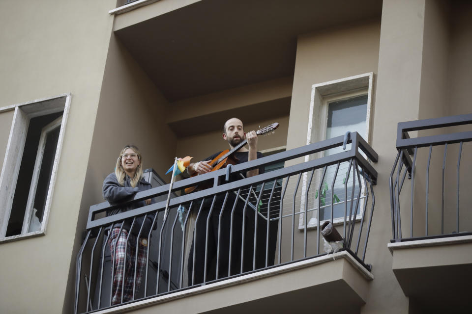 A man plays guitar on the balcony of his home during a flash mob launched throughout Italy to bring people together and try to cope with the emergency of coronavirus, in Milan, Italy, Friday, March 13, 2020. Italians have been experiencing yet further virus-containment restrictions after Premier Giuseppe Conte ordered restaurants, cafes and retail shops closed after imposing a nationwide lockdown on personal movement. For most people, the new coronavirus causes only mild or moderate symptoms. For some it can cause more severe illness. (AP Photo/Luca Bruno)