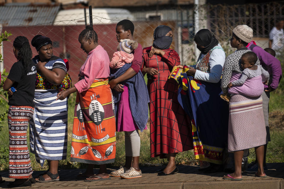 FILE- In this file photo taken Thursday, April 30, 2020, Women carrying their children lineup to receive vegetables from the Jan Hofmeyer community services in the Vrededorp neighborhood of Johannesburg. South Africa is struggling to balance its fight against the coronavirus with its dire need to resume economic activity. The country with the Africa’s most developed economy also has its highest number of infections — more than 19,000. (AP Photo/Jerome Delay, file)