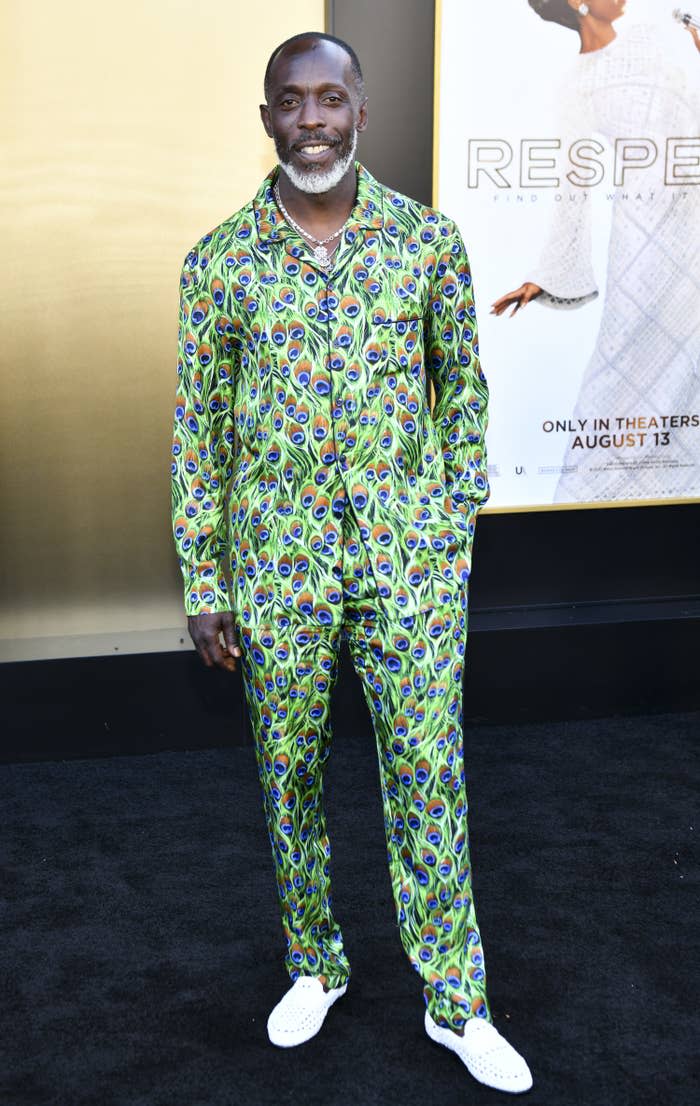 Michael K. Williams smiling while on the red carpet of an event as he poses in a peacock feather print shirt and pants