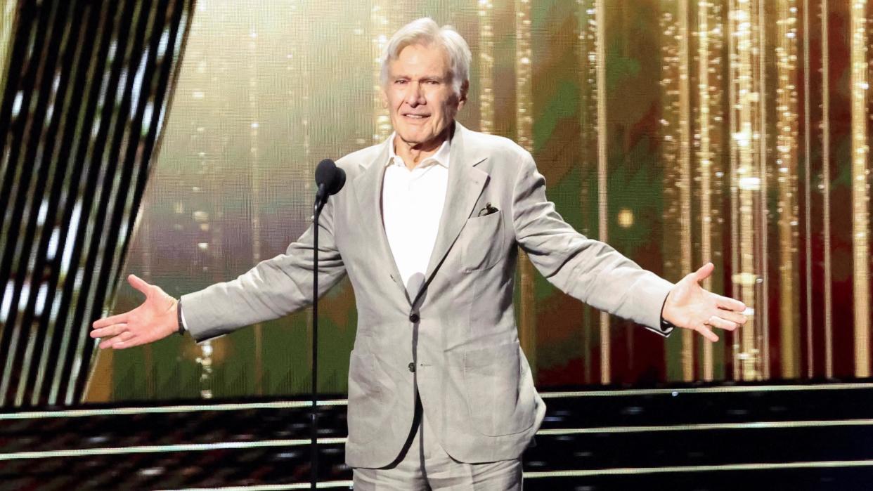 Harrison Ford gestures as he is honoured at the 2024 Disney Legends Awards during Disney's D23 Expo in Anaheim. Harisson is an 82-year-old man with grey hair. He wears a pale grey suit over a white shirt and stands on stage with his arms outstretched