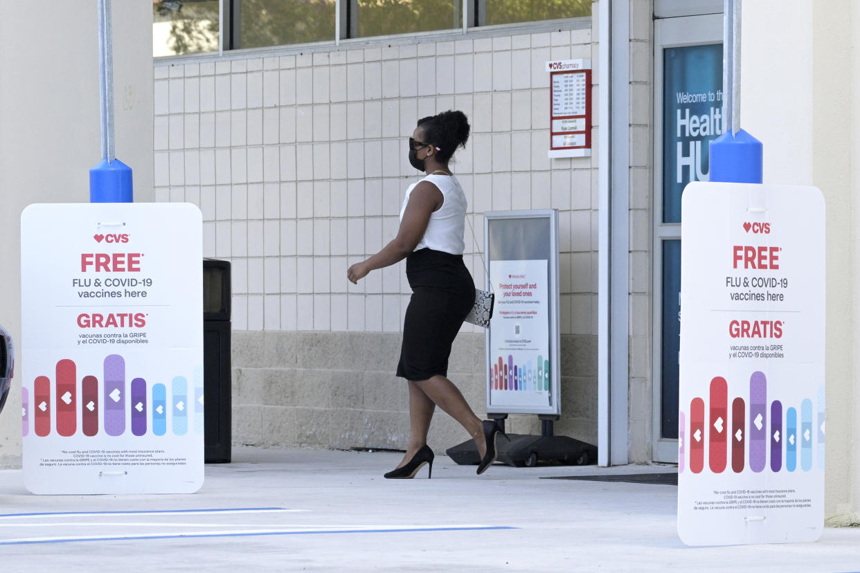 A woman walks past signs advertising free flu shots and COVID-19 vaccines (Phelan M. Ebenhack via AP file)