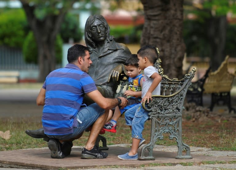 A man with his sons sit next to a statue of John Lennon in a park in Havana, on March 11, 2017