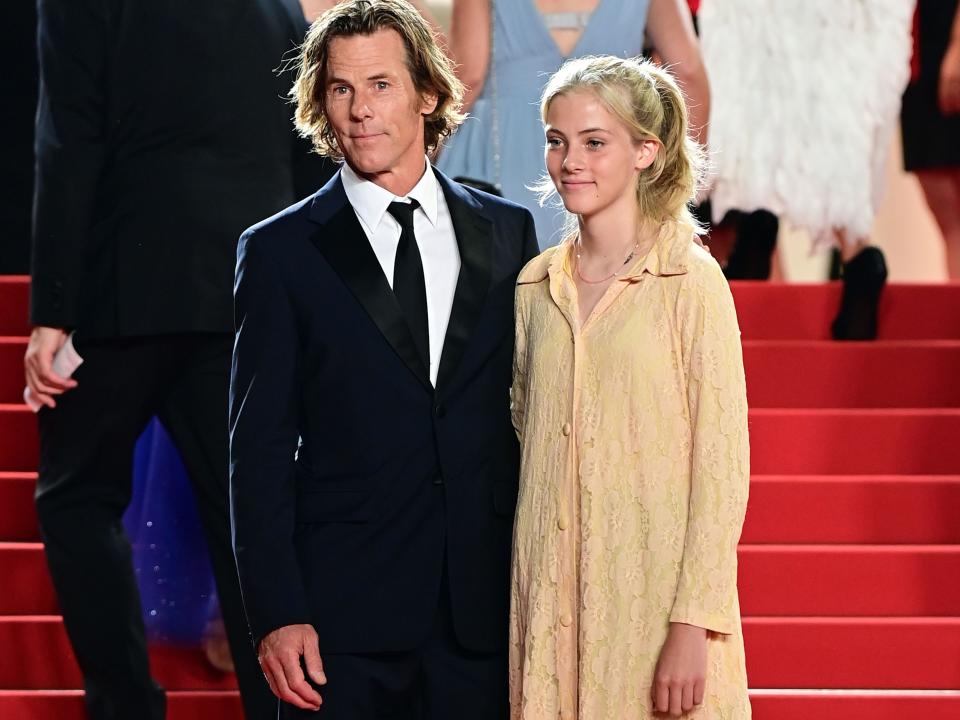 Cinematographer Daniel Moder wears a black suit and poses on the red carpet at Cannes with daughter Hazel, in a yellow dress and black shoes.