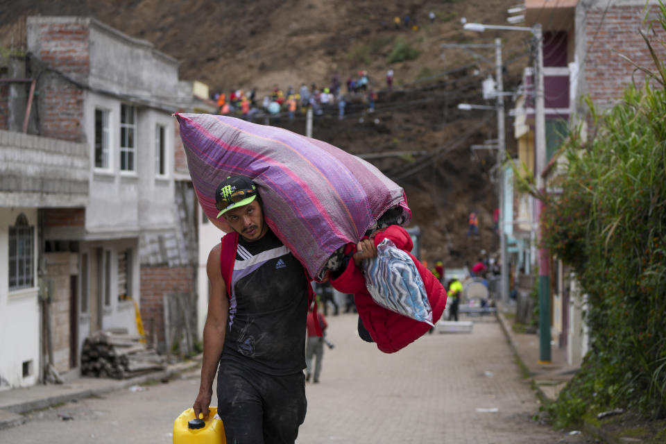 A resident carries household belongings in Alausi, Ecuador, Tuesday, March 28, 2023, a day after the landslide swept through the town burying dozens of homes killing at least seven people. (AP Photo/Dolores Ochoa)