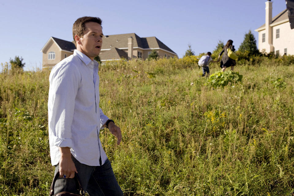 A scared man stands in a field while a woman and her son run to a nearby house