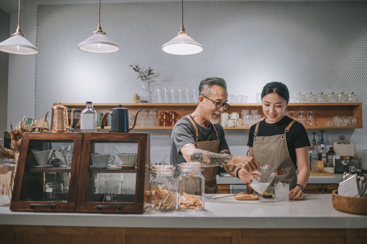 asian chinese senior male barista teaching his daughter making coffee at cafe counter