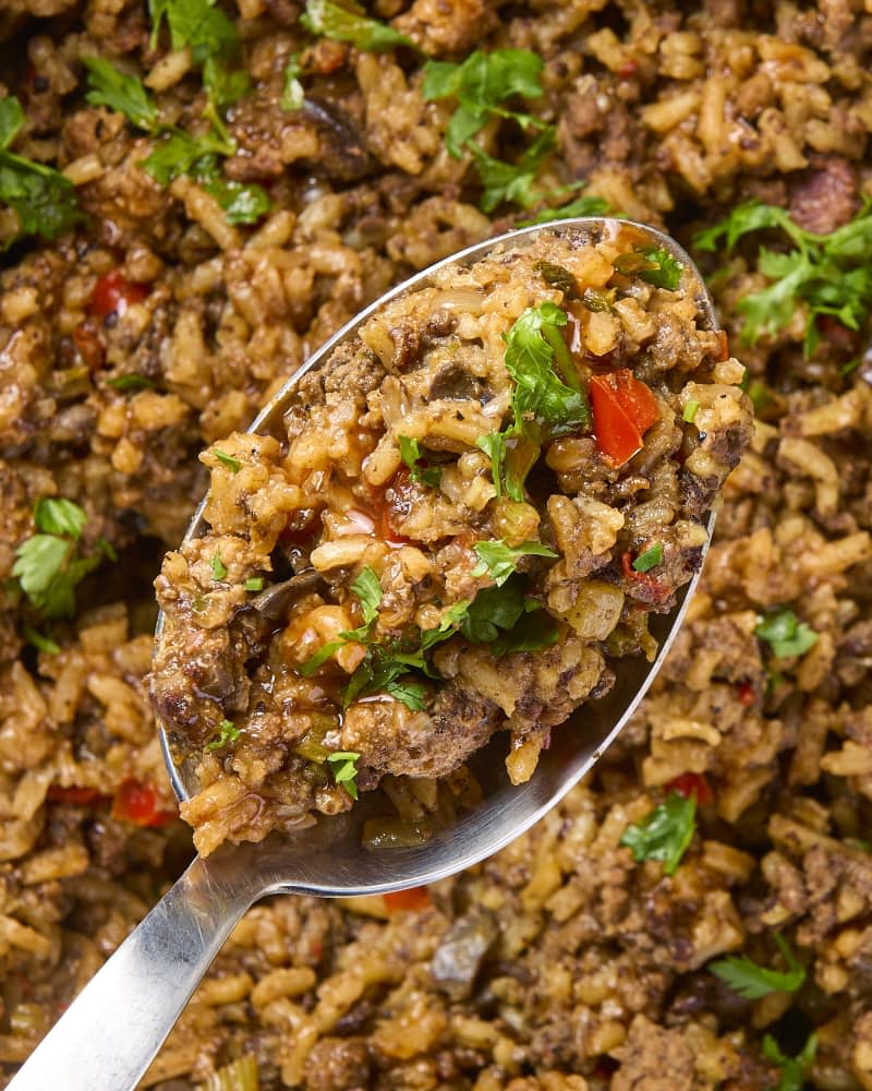 Close up photo of a spoon full of dirty rice topped with hot sauce.