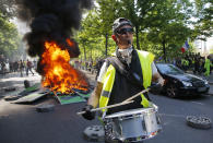 A man bangs a drum in front of a fire on the street during a yellow vest demonstration in Paris, Saturday, April 20, 2019. French yellow vest protesters are marching anew to remind the government that rebuilding the fire-ravaged Notre Dame Cathedral isn't the only problem the nation needs to solve. (AP Photo/Michel Euler)