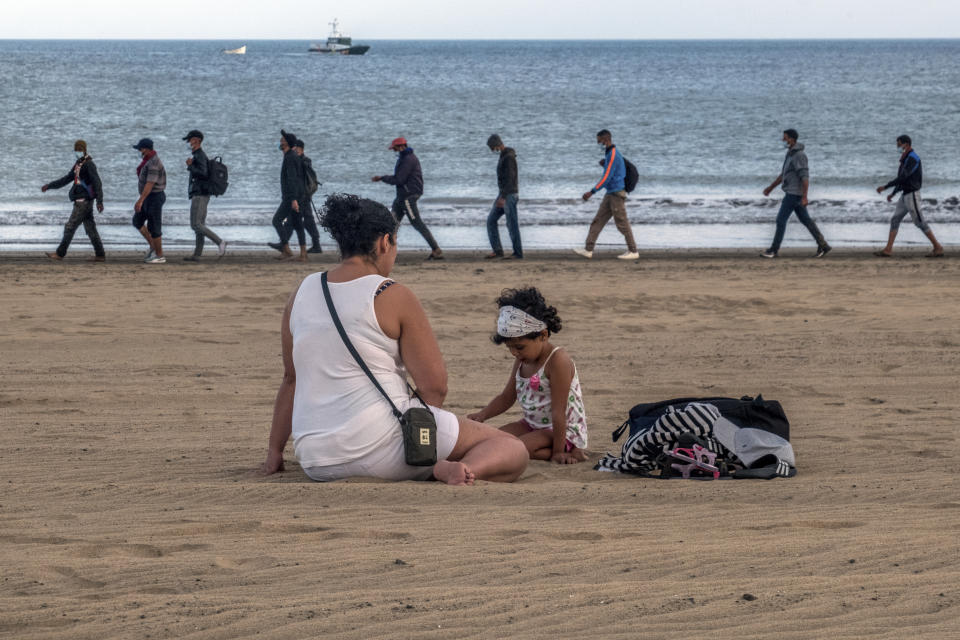 Migrants from Morocco walk along the shore escorted by Spanish Police after arriving at the coast of the Canary Island, crossing the Atlantic Ocean sailing on a wooden boat on Tuesday, Oct.20, 2020. Some 1,000 migrants have spent the night again sleeping in emergency tents in a dock while authorities in the Canary Islands complain that the Spanish government keeps blocking transfers of newly arrived migrants to the mainland over coronavirus concerns. (AP Photo/Javier Bauluz)