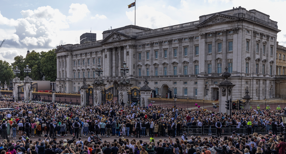 A shot of the front gates of Buckingham Palace with a large crowd in front of it.