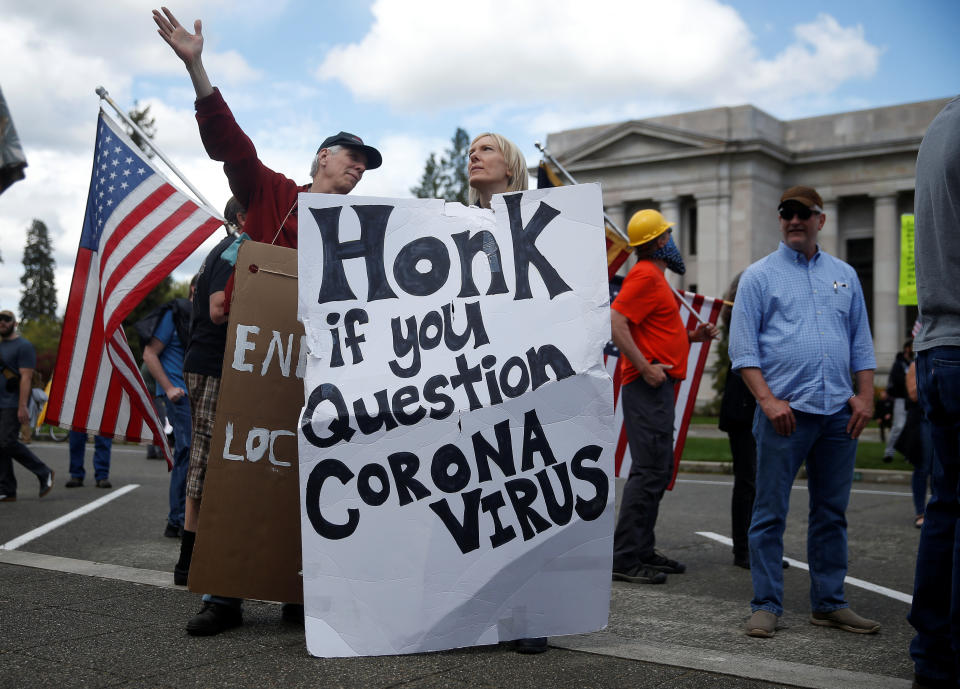 A woman with a sign questioning coronavirus talks with another protester at the Capitol building in Olympia, Washington.