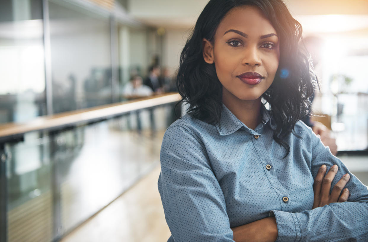 Pretty young dreamy African-American office worker standing with arms crossed and looking at camera.