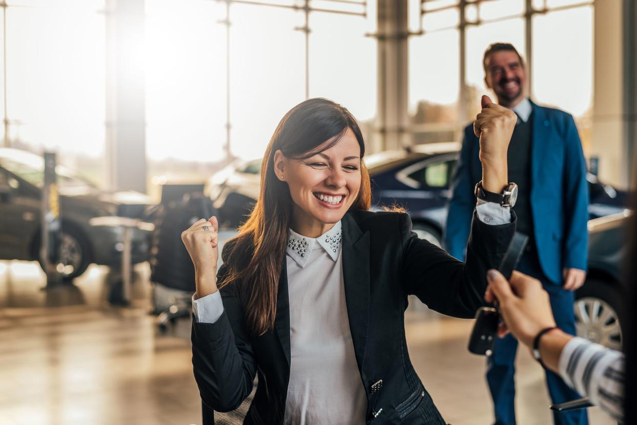 cheerful young woman receiving the keys of her new car at car dealership