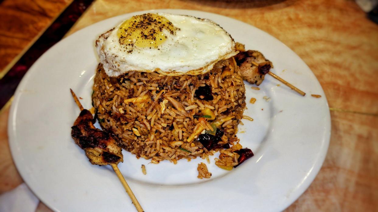 Nasi goreng on a white plate with two pieces of grilled chicken on sticks.