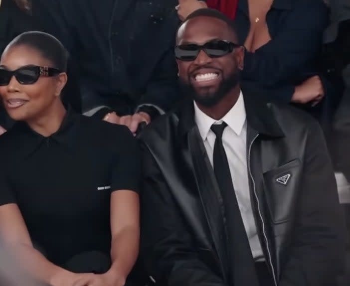 Dwyane smiles wide while sitting in the front row next to Gabrielle