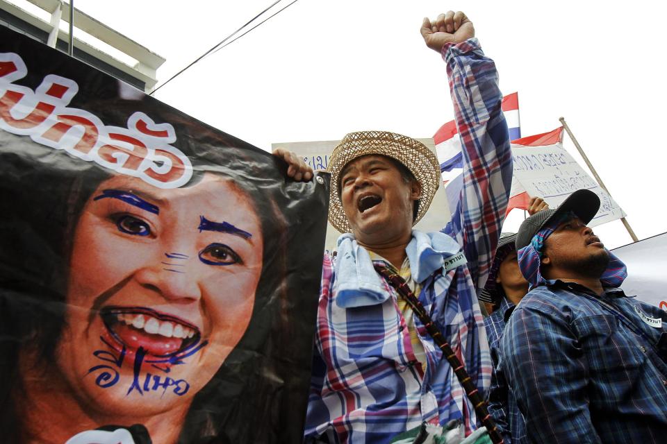 Farmers hold a defaced poster of Thai PM Yingluck as they protest outside her temporary office in Bangkok