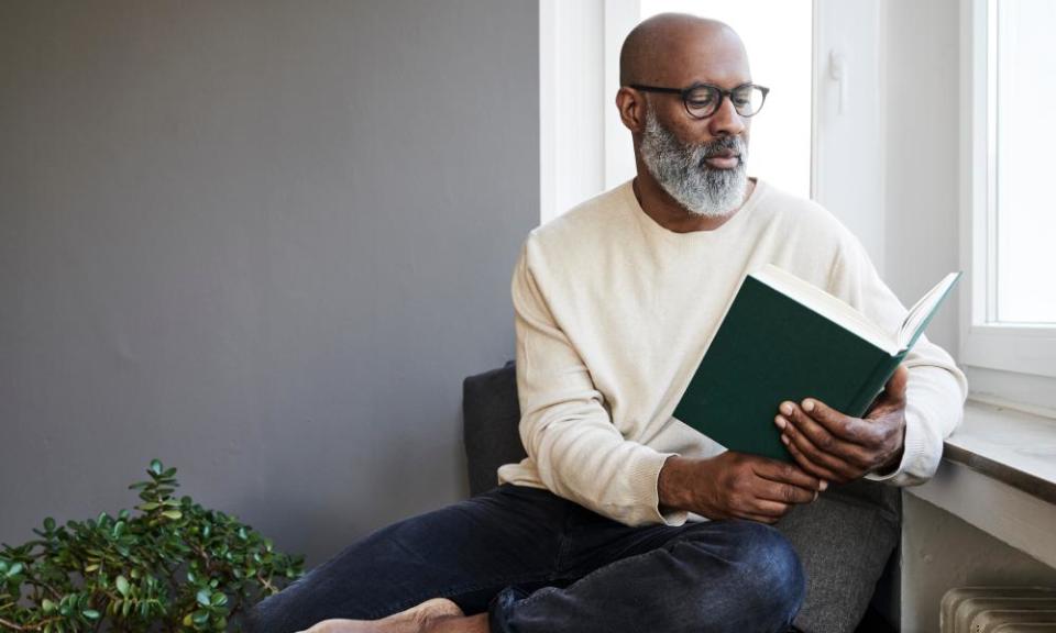 Mature man sitting at window, reading a book