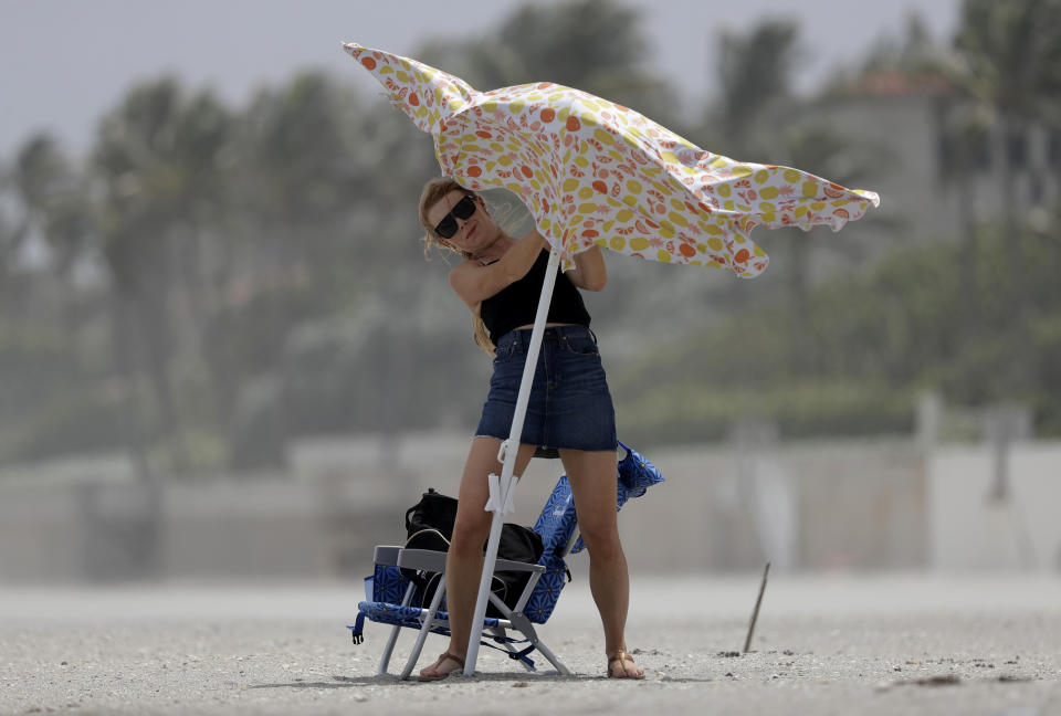 Una bañista intenta colocar una sombrilla de playa el sábado 1 de agosto de 2020 en Palm Beach, Florida. El huracán Isaías se dirige a la costa de Florida, donde las autoridades cerraron playas, parques y puestos de pruebas de coronavirus. (AP Foto/Wilfredo Lee)