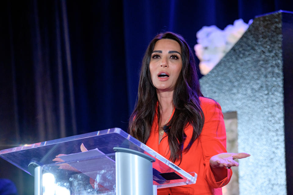 Marisol Nichols speaks at a podium during an event with a decorative backdrop