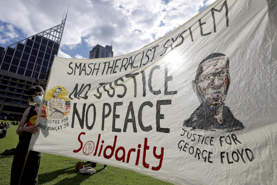 A man holds a banner showing George Floyd as thousands gather at a rally supporting the Black Lives Matter and Black Deaths in Custody movements in Sydney, Sunday, July 5, 2020. (AP Photo/Rick Rycroft)