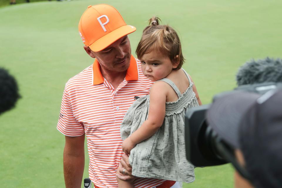 Rickie Fowler carries his daughter Maya as he is being interviewed after winning the Rocket Mortgage Classic at Detroit Golf Club in Detroit on Sunday, July 2, 2023.
