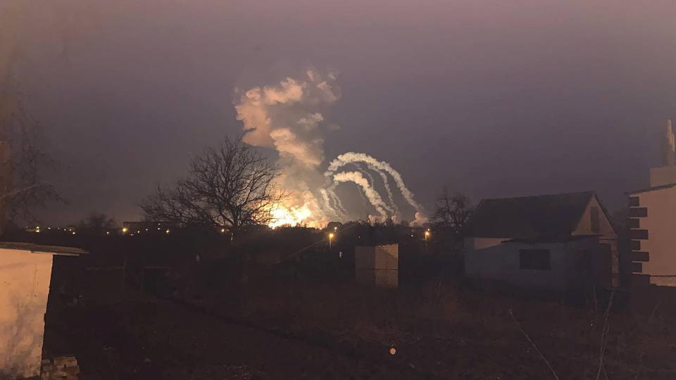 A major explosion against a twilit sky, with trails of smoke.