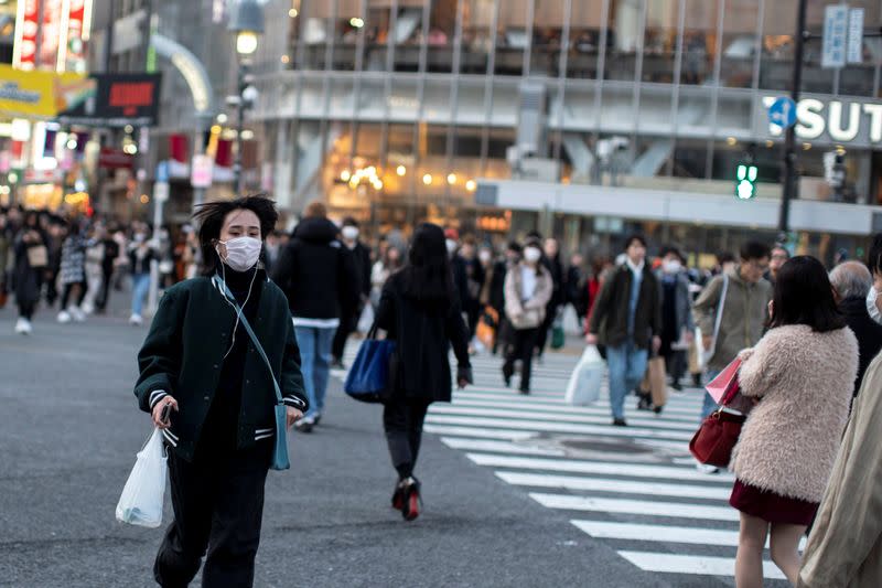 A woman wearing a protective face mask runs across a street at Shibuya in Tokyo