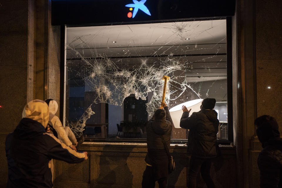 Demonstrators smash the window of a bank following a protest condemning the arrest of rap singer Pablo Hasel in Barcelona, Spain, Thursday, Feb. 18, 2021. The imprisonment of Pablo Hasel for inciting terrorism and refusing to pay a fine after having insulted the country's monarch has triggered a social debate and street protests. (AP Photo/Felipe Dana)