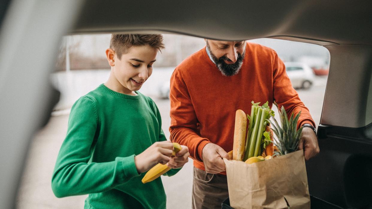 Father and son putting bags in trunk of car.