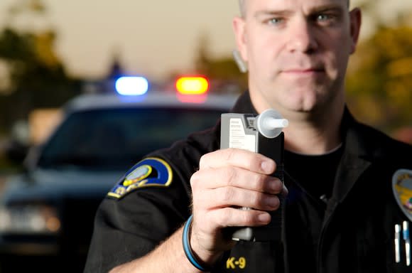 A law enforcement officer holding a breathalyzer device.
