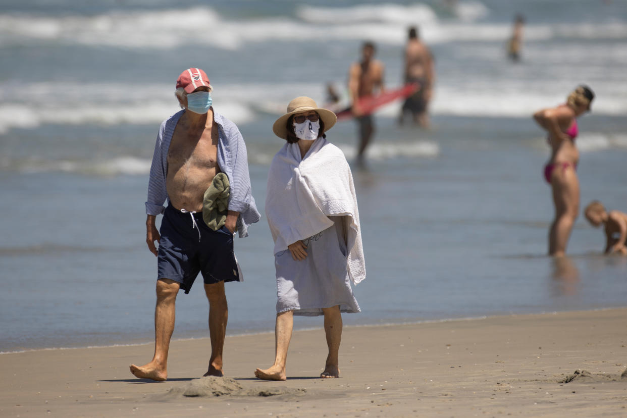 People wearing face masks walk along the beach as California reported its largest number of new coronavirus infections in a single day, during the outbreak of the coronavirus disease (COVID-19) in Del Mar, California, U.S., July 15, 2020. REUTERS/Mike Blake