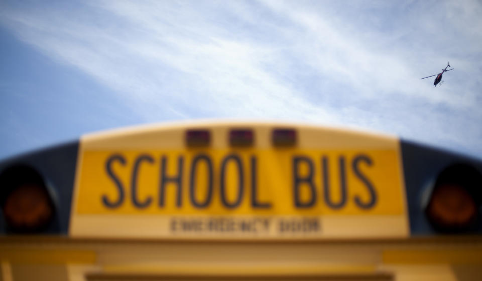 <p>A police helicopter hovers over a school bus as it drops off children outside a subdivision May 16, 2012, in Hampton, Ga. Police in an Atlanta suburb are escorting school buses and guarding students at bus stops after a man aimed a rifle at a bus with children on board and dropped a notebook that listed bus numbers. (AP Photo/David Goldman) </p>