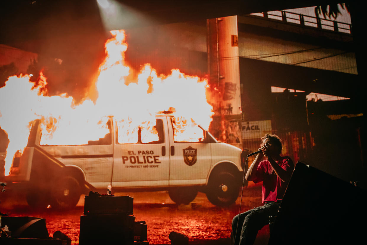 Zack de la Rocha, vocalista de la banda Rage Against the Machine, se presenta frente a una pantalla que muestra imágenes de una camioneta policial en llamas, en el United Center en Chicago, el 11 de julio de 2022.  (Jamie Kelter Davis/The New York Times)
