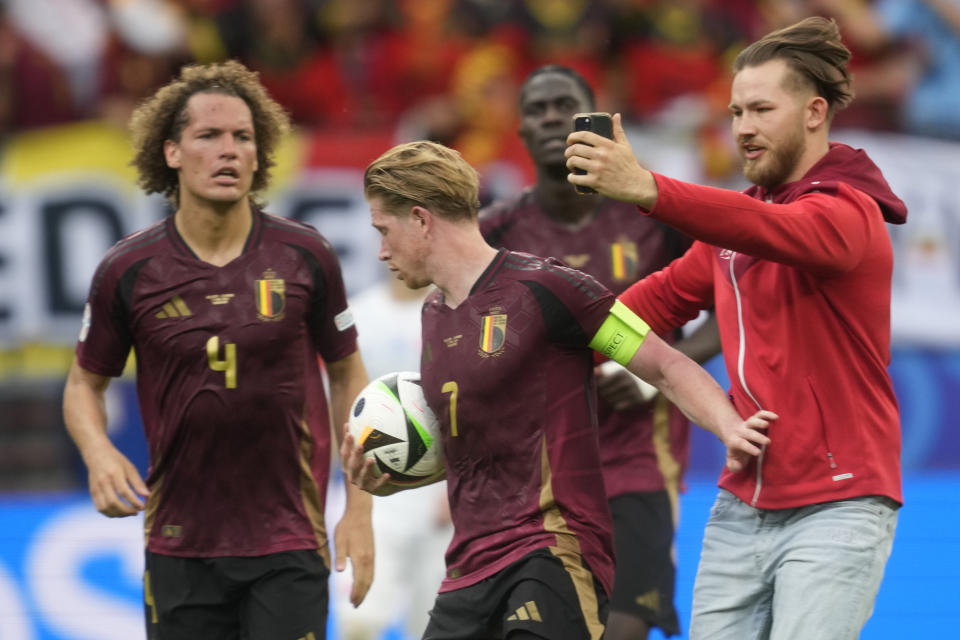 A pitch invader, right, tries to take a selfie with Belgium's Kevin De Bruyne during a Group E match between Belgium and Slovakia at the Euro 2024 soccer tournament in Frankfurt, Germany, Monday, June 17, 2024. (AP Photo/Michael Probst)