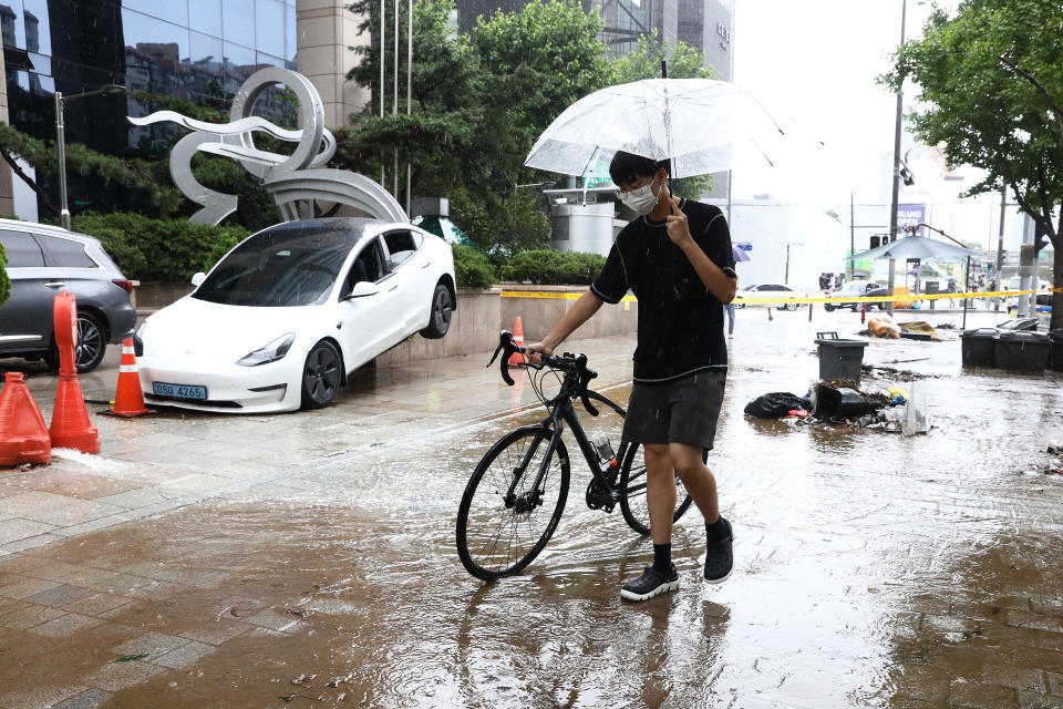 A man with a bicycle walks along a street that was still draining after heavy rainfall in Seoul on Tuesday.