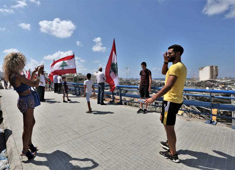People stand next to Lebanese flags on a bridge overlooking the damaged Beirut port and grain silos, in Beirut, Lebanon.