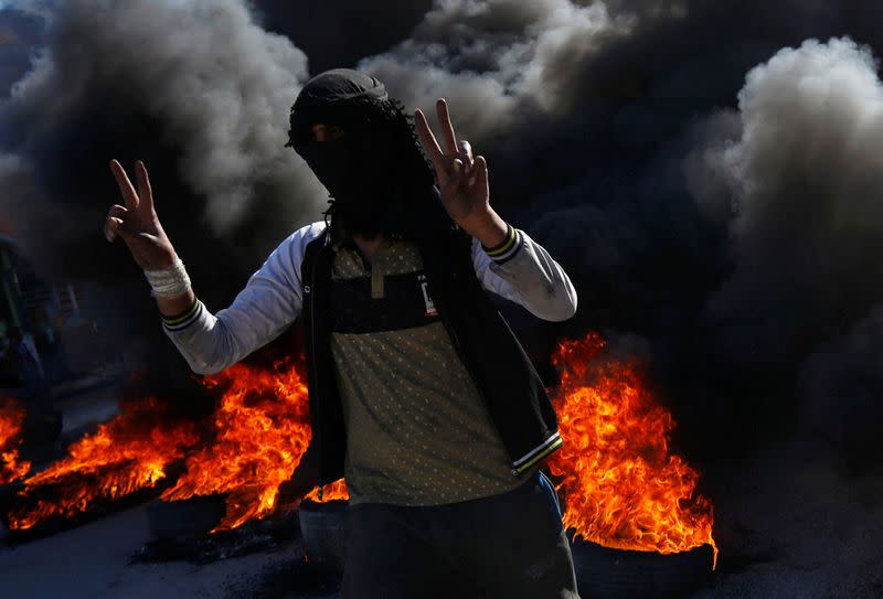 An Iraqi demonstrator gestures as they burn tires to block a road during ongoing anti-government protests in Najaf