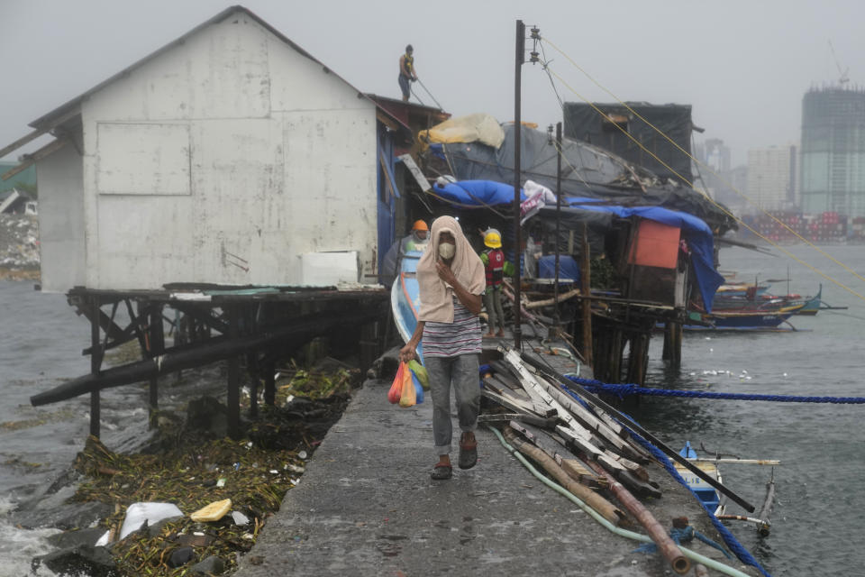 A man carries bags of food while another reinforces their roof as they prepare for the coming of Typhoon Noru in Manila, Philippines, Sunday, Sept. 25, 2022. The powerful typhoon shifted and abruptly gained strength in an "explosive intensification" Sunday as it blew closer to the northeastern Philippines, prompting evacuations from high-risk villages and even the capital, which could be sideswiped by the storm, officials said. (AP Photo/Aaron Favila)