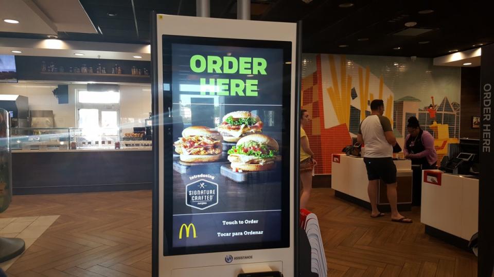 <p>Giant kiosks implore you to “order here,” on electronic touch screens. </p>