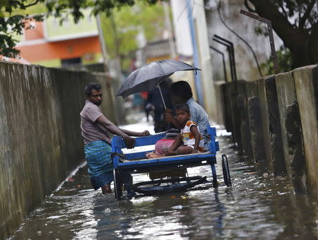 A man carries his family on a rickshaw cart as he wades through a flooded street in Chennai, India, December 5, 2015. REUTERS/Anindito Mukherjee