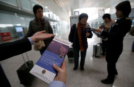 Quarantine officials distribute leaflets explaining the Ebola virus and its symptoms to passengers at a departure terminal of the Beijing Capital International Airport October 30, 2014. REUTERS/Kim Kyung-Hoon