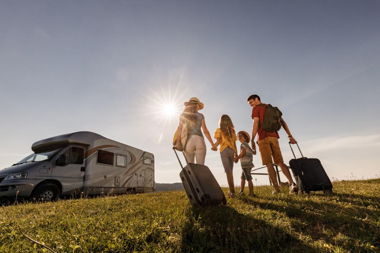 Low angle view of happy family holding hands while walking towards their camper trailer for a summer vacation. Copy space.