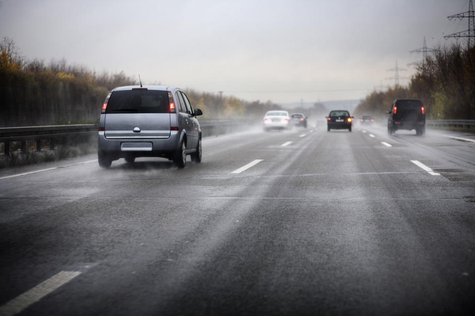 Cars being driven on a wet highway on a rainy day, with mist and water spray visible behind them