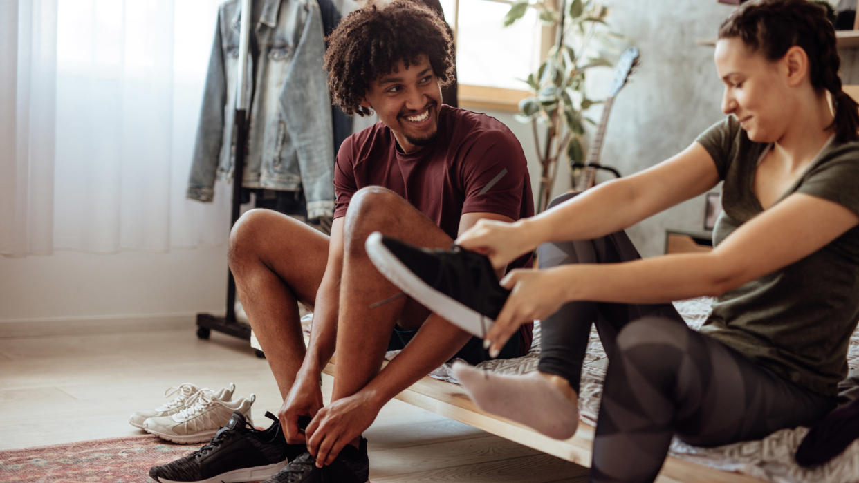  A young couple sitting on the edge of their bed, putting on trainers. 