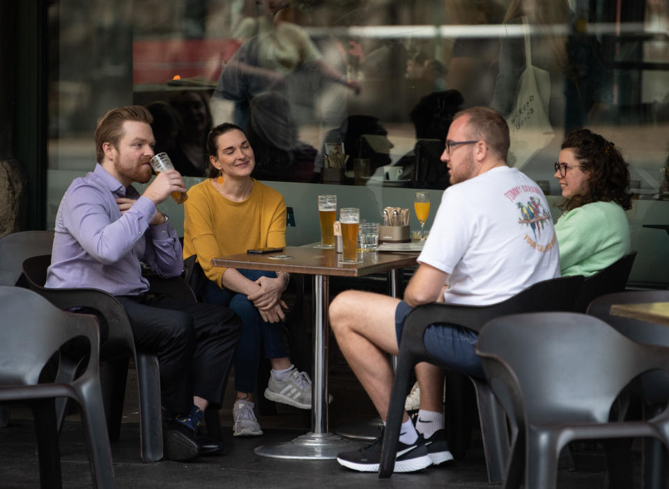 A group of four friends sit outside a bar drinking beer. 